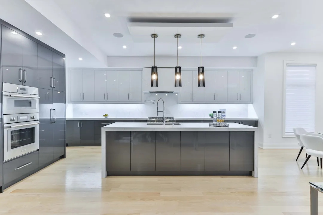 Modern kitchen with three black pendant lights over gray island, recessed ceiling lights, and glossy gray cabinets