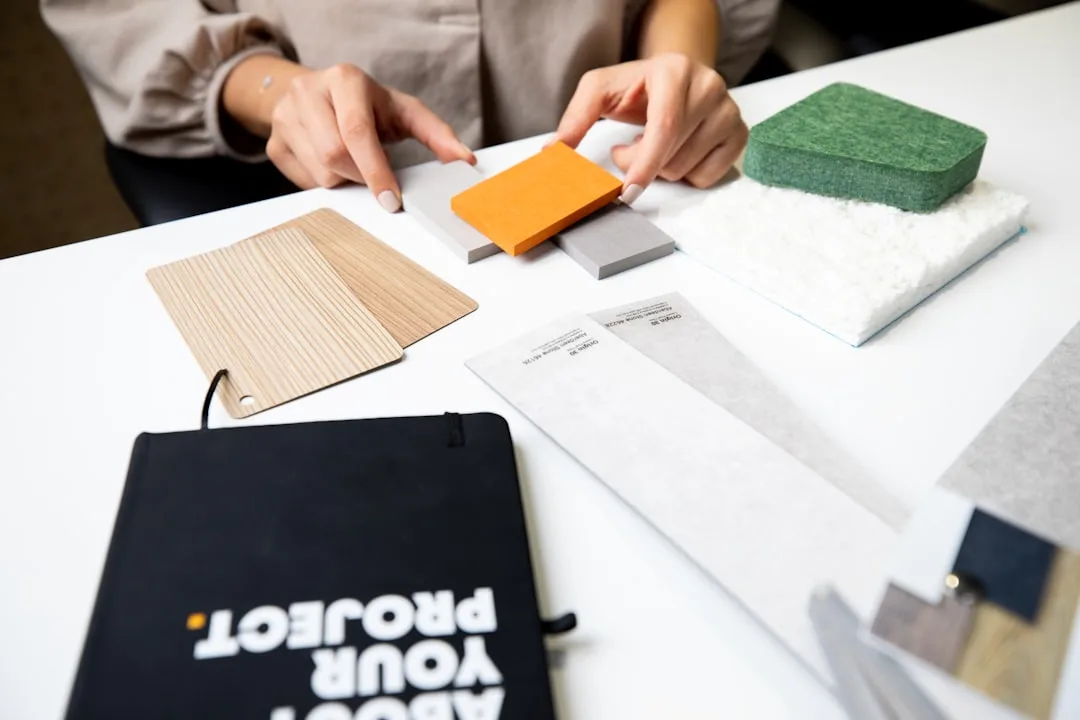 Interior designer arranging material swatches including wood, fabric, and color samples on a white table for a design pr