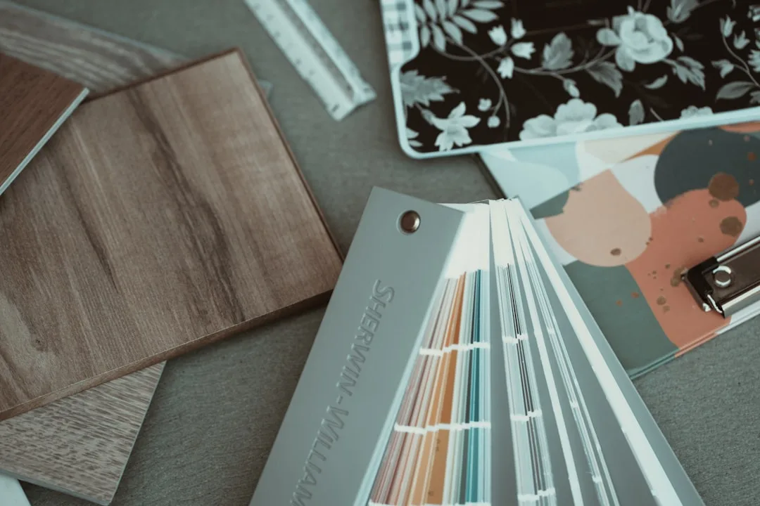 Sherwin-Williams paint color swatches fanned out next to wood flooring samples and wallpaper on a design desk