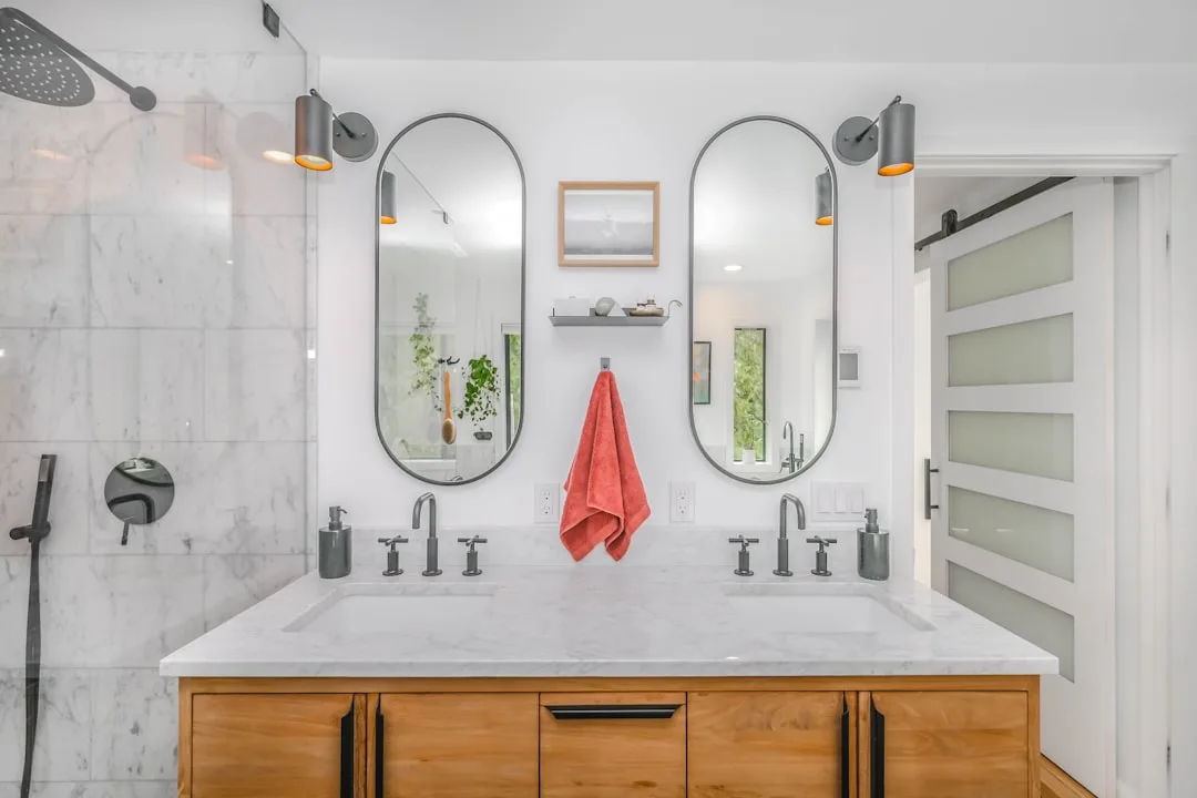Modern bathroom with sliding barn door alternative featuring frosted glass panels beside double vanity with oval mirrors