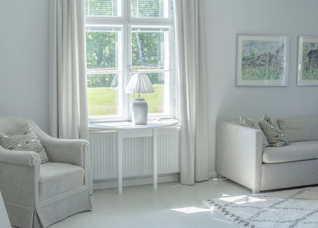 Bright Scandinavian living room with cool white walls, natural light from window, gray sofa and armchair