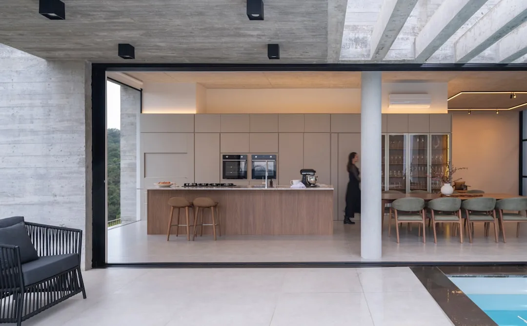 Open floor plan with distinct kitchen, dining, and outdoor zones separated by architectural elements and sliding glass w
