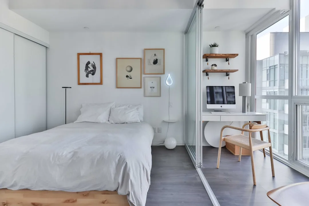 Small bedroom with glass partition separating white desk workspace and bed, minimalist Scandinavian guest room home offi