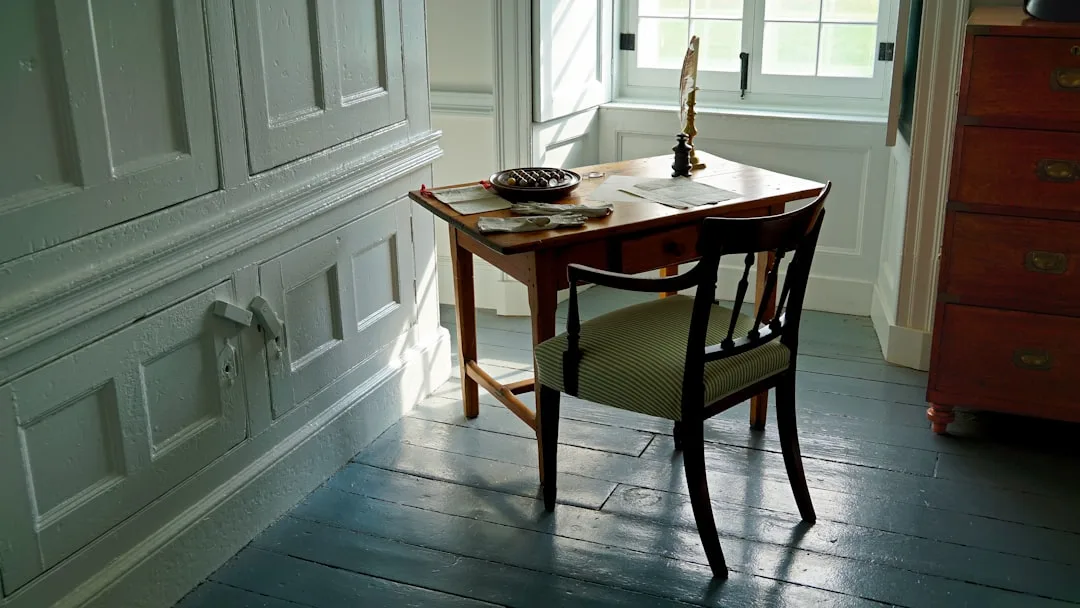 Antique wooden writing desk placed diagonally in a corner with natural window light in a historic room