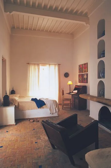 Moroccan bedroom with alcove desk workspace, terracotta tile floor, white walls, and wooden writing desk with lamp