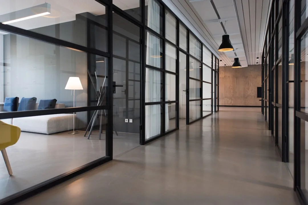 Modern office hallway with glass partition walls, concrete floors, and pendant lighting for a sleek workspace design