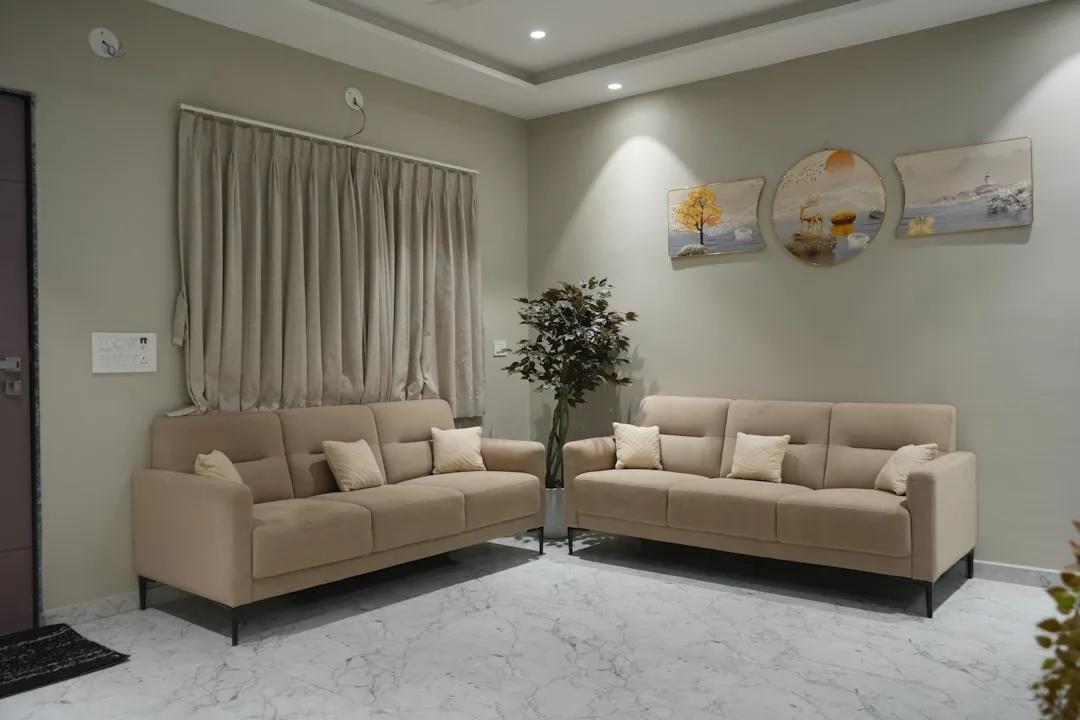 Two beige sofas facing each other in a modern living room with marble floors and neutral wall decor