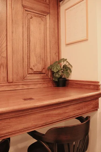 Wooden cloffice conversion with built-in desk, carved cabinet door, small monstera plant and framed wall art