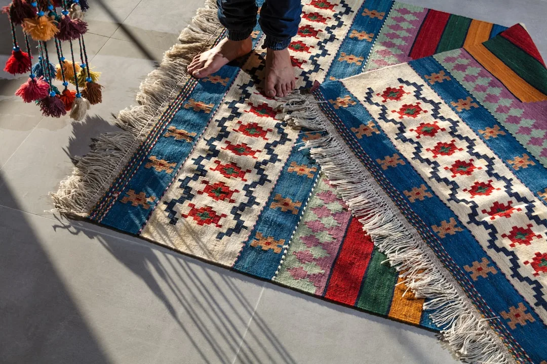 Person standing barefoot on a colorful traditional kilim rug with fringe and geometric patterns on a tiled floor