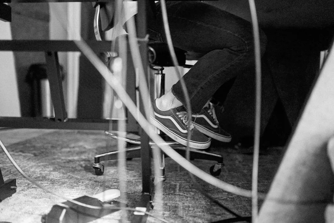 Tangled cables under office desk chair with Vans sneakers visible, illustrating poor cable management in workspace