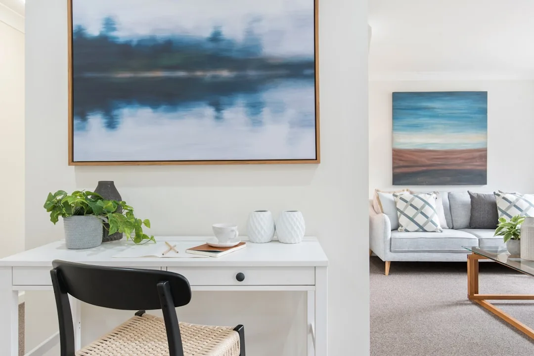 White home office desk with large framed abstract landscape painting above it styled with plants and white vases