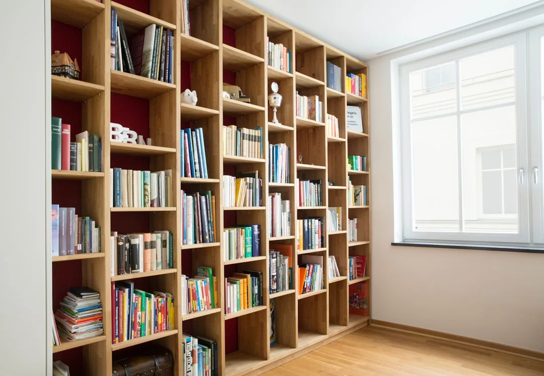 Large floor-to-ceiling open wooden bookshelf with colorful books used as a room divider in a modern home office