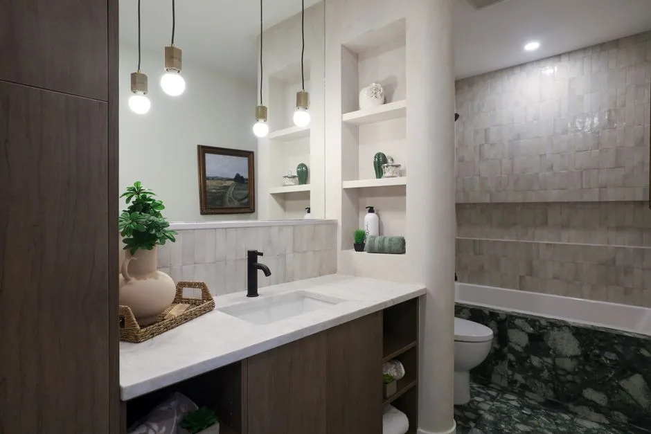 Modern bathroom accent wall with handmade zellige tiles, green marble floor, built-in shelves, and wood vanity with blac