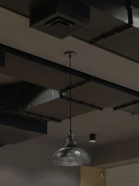 Industrial pendant light with glass dome shade hanging from ceiling with exposed ductwork and black metal beams