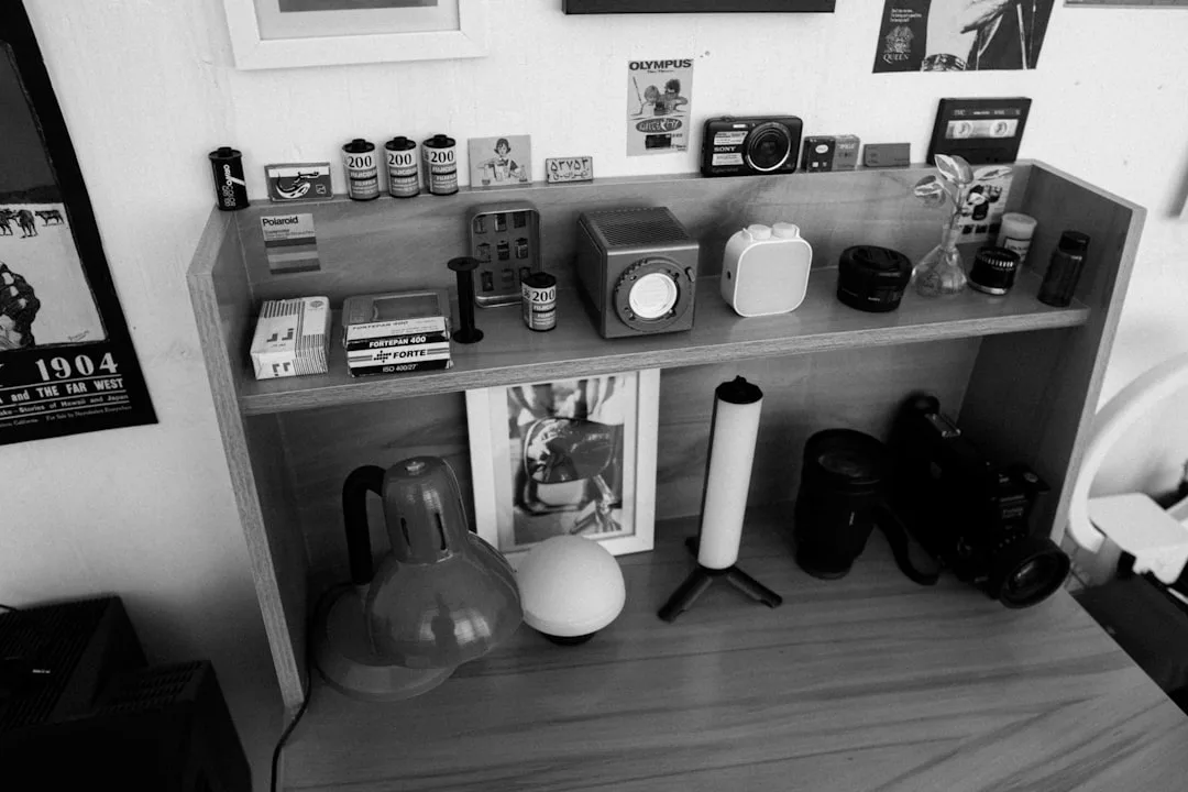 Wooden desk shelf unit organized with cameras, film rolls, and personal items in a home workspace setup