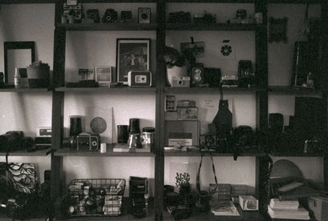 Vintage shelf unit filled with cameras, collectibles, and personal items showing functional yet eclectic storage organiz