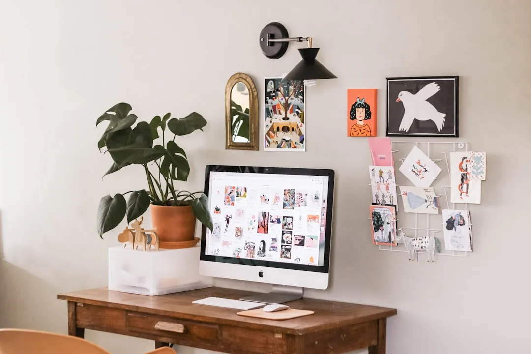 Small home office with built-in wooden desk, iMac computer, monstera plant, and wall art gallery in compact workspace
