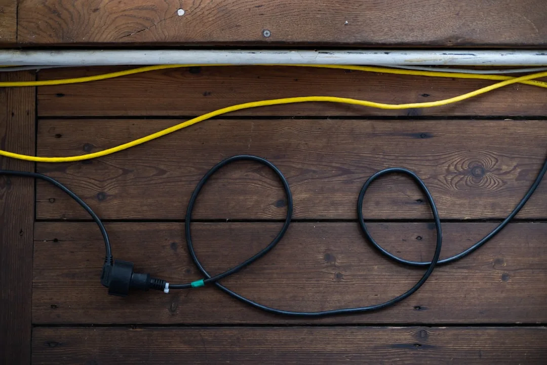 Black extension cord with plug and yellow cable lying loosely on wooden floor boards