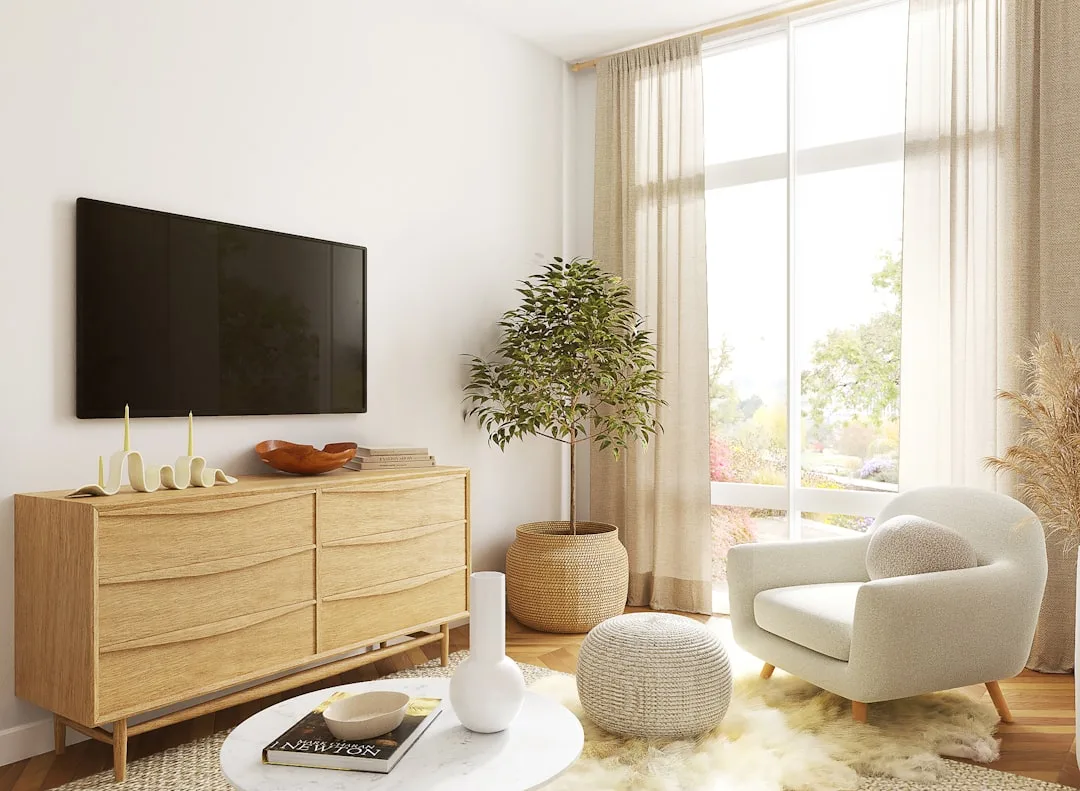 Scandinavian living room with wall-mounted TV above wooden dresser, white armchair, and indoor plant by large window