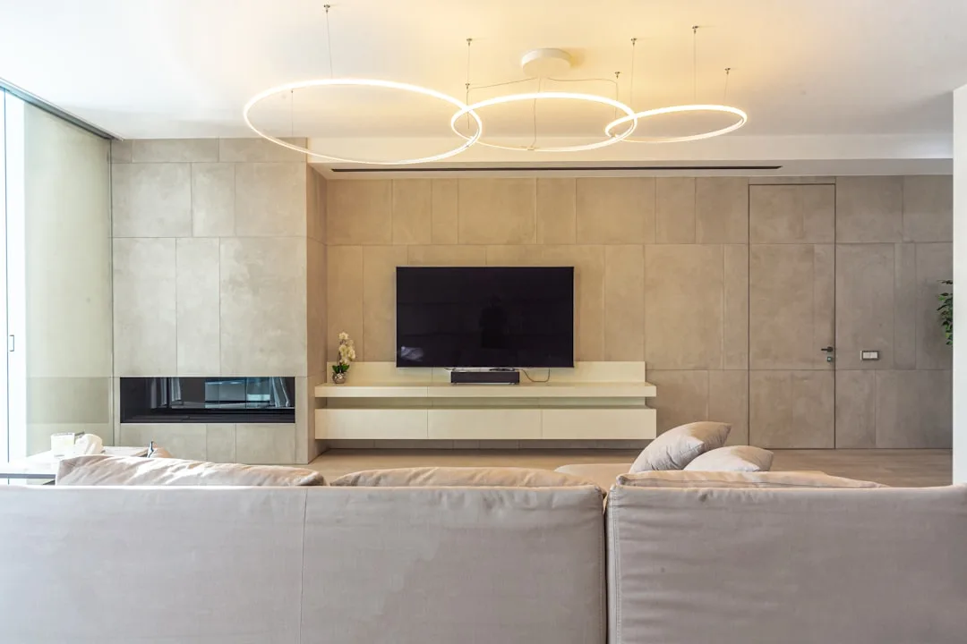Modern living room TV wall with circular LED pendant light fixtures illuminating a minimalist concrete accent wall