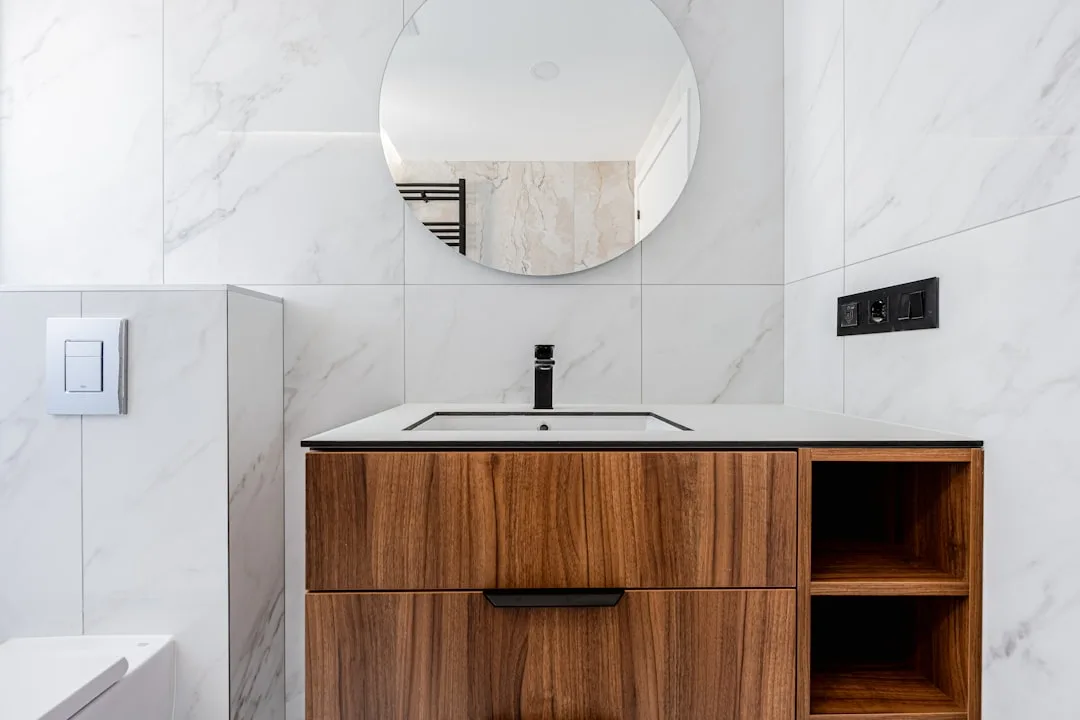 Floating walnut bathroom vanity with open side shelving, black faucet, and white marble tile walls