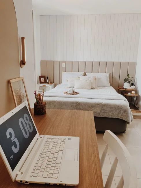 Neutral bedroom with upholstered headboard, white bedding, and wooden desk with laptop showing 3:08 PM