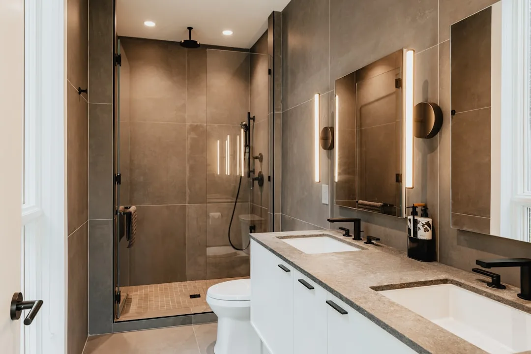 Modern bathroom with dark grout large-format tiles, glass shower enclosure, white double vanity with stone countertop