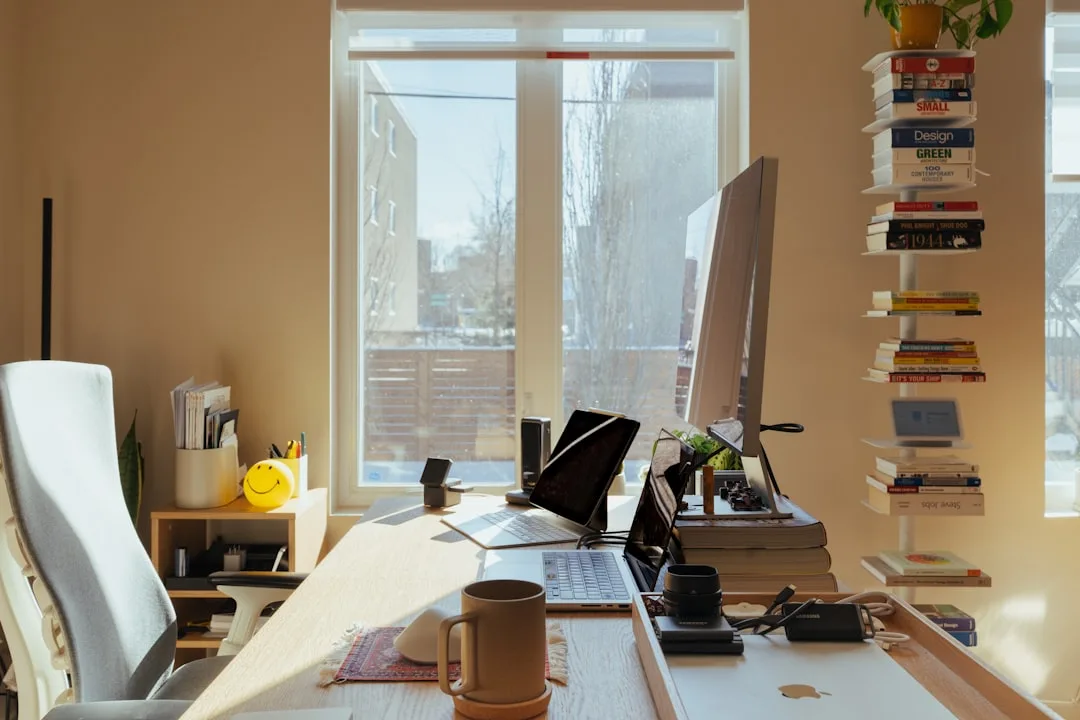 Ergonomic home office desk setup with iMac monitor, laptop, and office chair in sunlit workspace