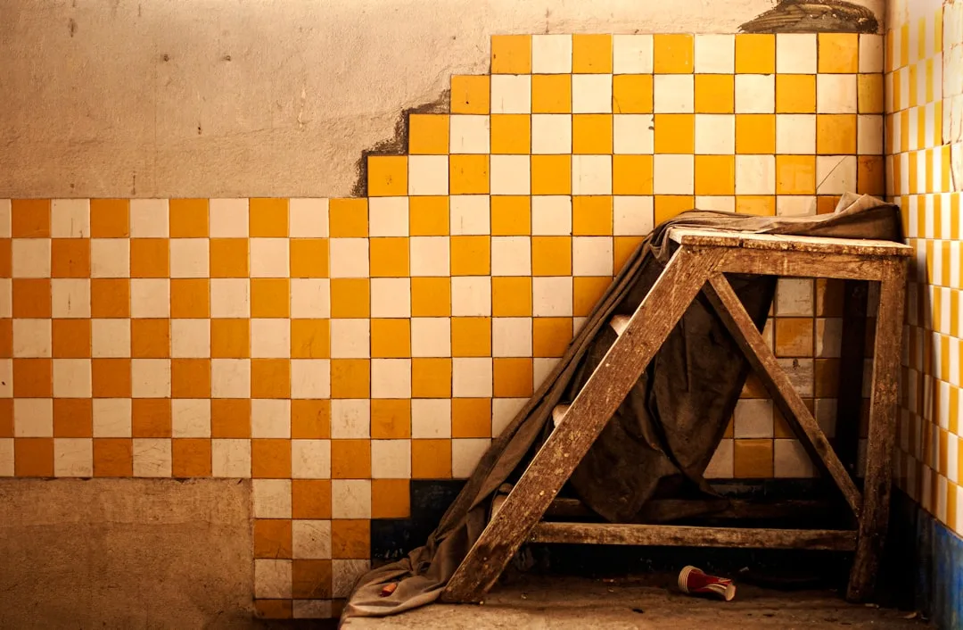 Abandoned bathroom with checkered orange and white tiles showing installation mistakes and worn wooden step stool