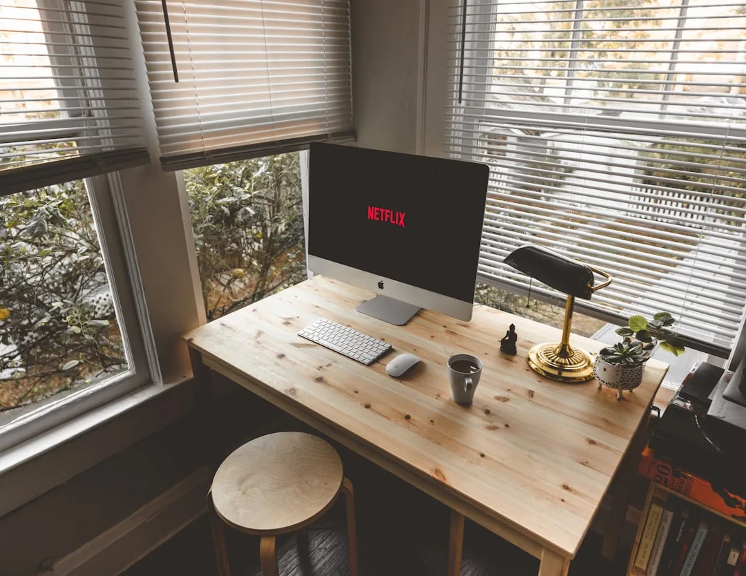 Small-space home office nook with iMac, wireless keyboard, mouse, desk lamp, and succulent on a wooden desk by windows