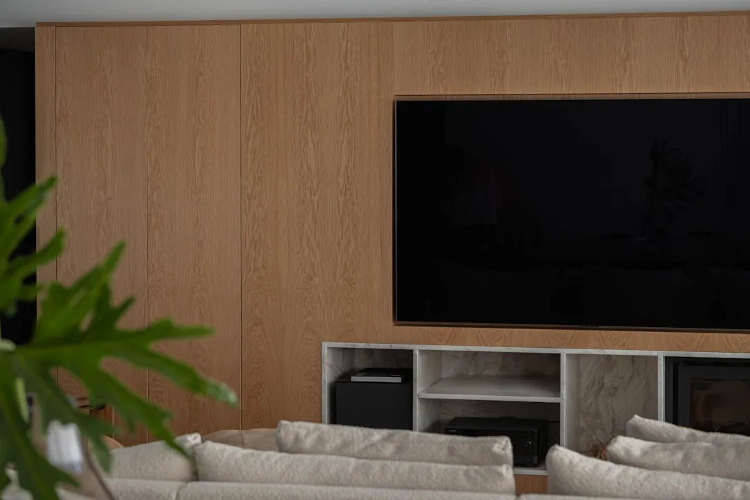 Large flat-screen TV recessed into a floor-to-ceiling oak wood panel wall above a marble media console in a modern livin