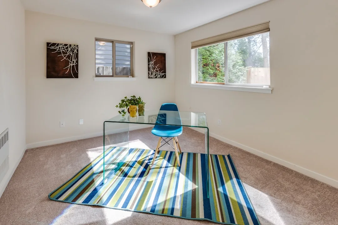 Home office with glass desk, blue Eames chair, and